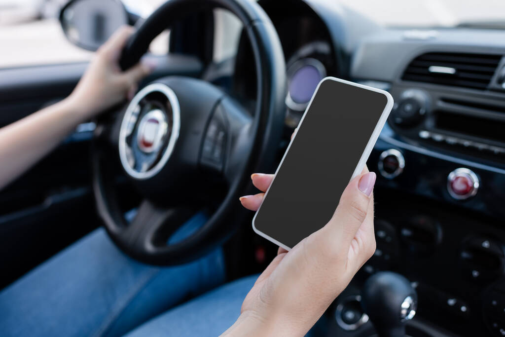 Cropped view of blurred woman holding smartphone with blank screen in blurred car  - Foto, imagen