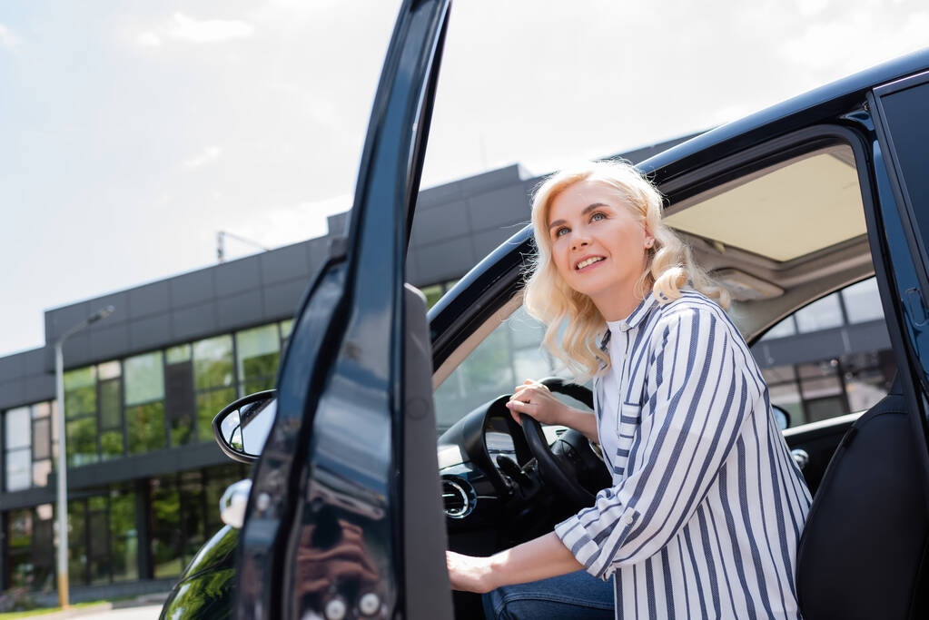 Smiling woman opening door of car and looking away outdoors  - Fotografie, Obrázek