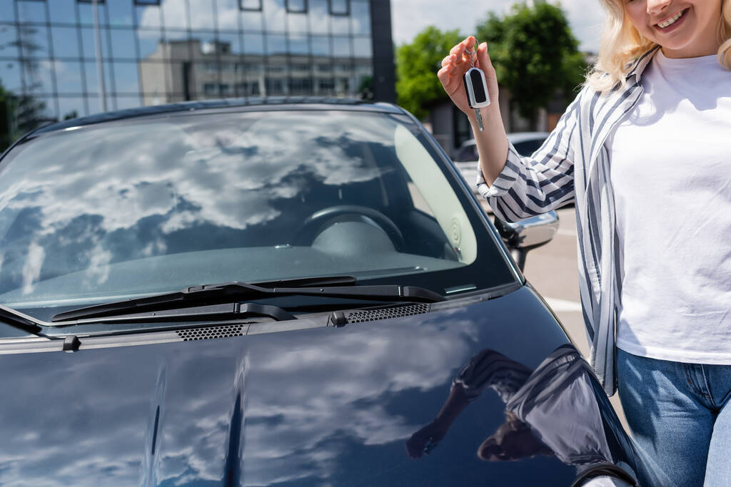 Cropped view of smiling woman holding key near car outdoors  - Photo, image