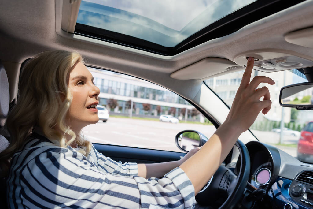 Blonde driver in casual clothes pushing button in car  - Foto, imagen