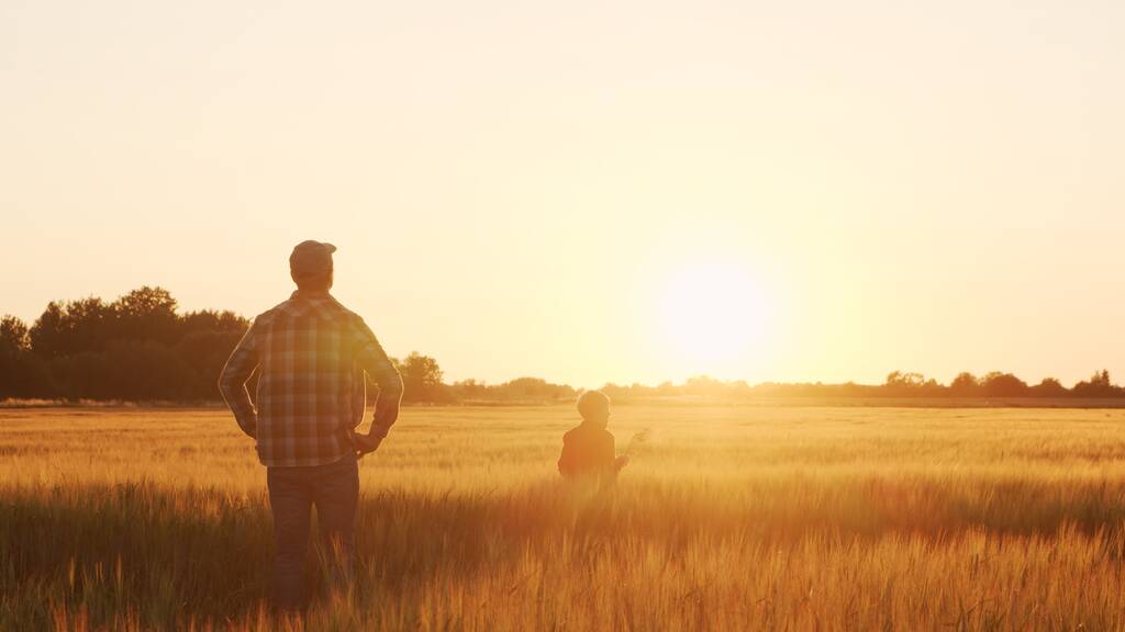 Farmer and his son in front of a sunset agricultural landscape. Man and a boy in a countryside field. The concept of fatherhood, country life, farming and country lifestyle. - 写真・画像