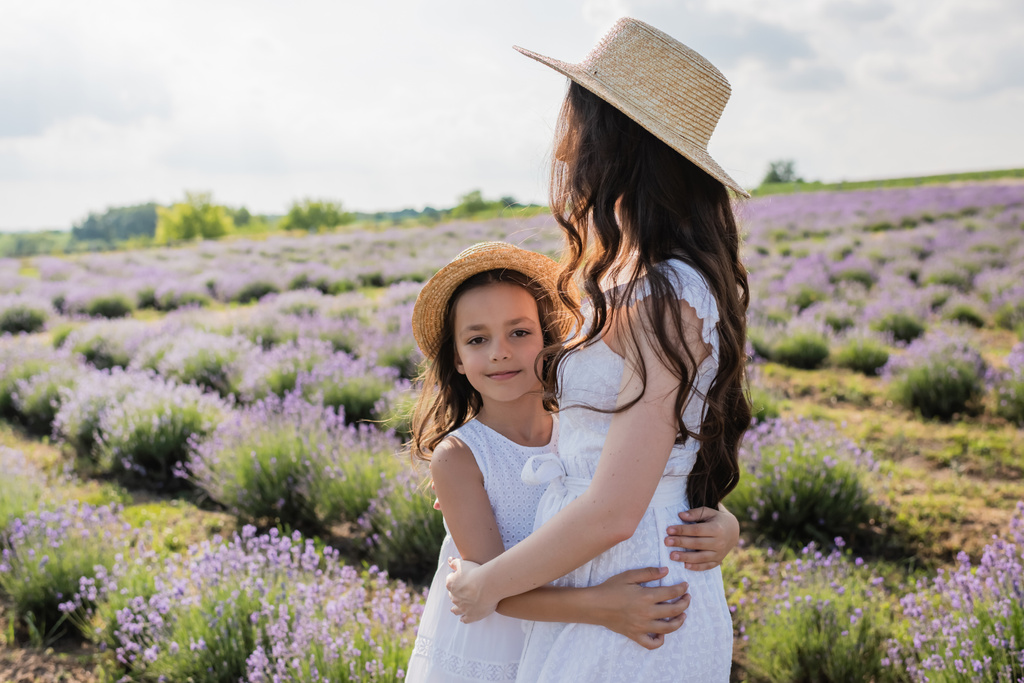 happy child in white dress embracing mom in lavender field - Foto, afbeelding
