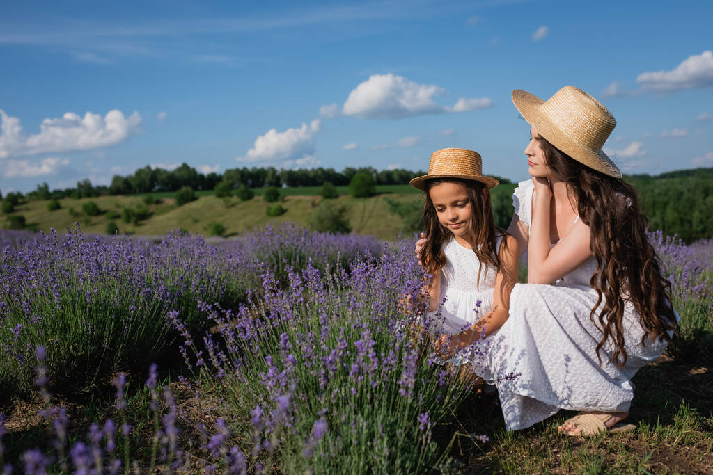 woman and child in straw hats and white dresses near blooming lavender in meadow - Zdjęcie, obraz