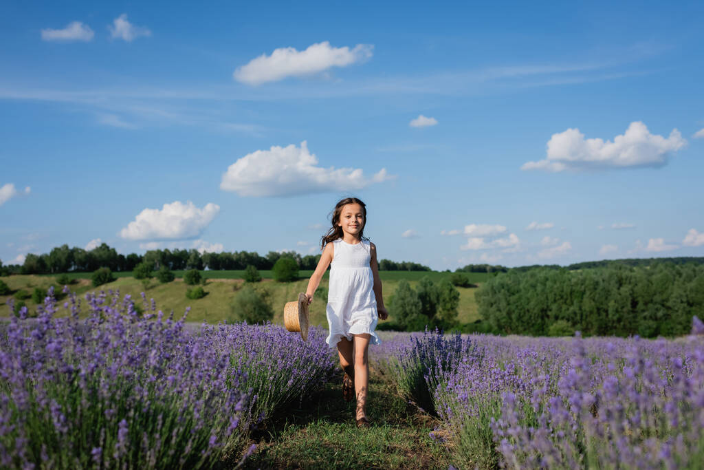 full length of smiling girl in white summer dress walking in meadow of blooming lavender - Fotó, kép