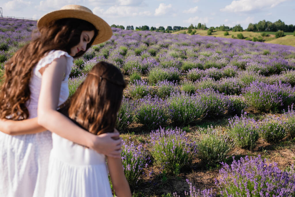 brunette woman hugging daughter in lavender field on blurred foreground - Foto, afbeelding