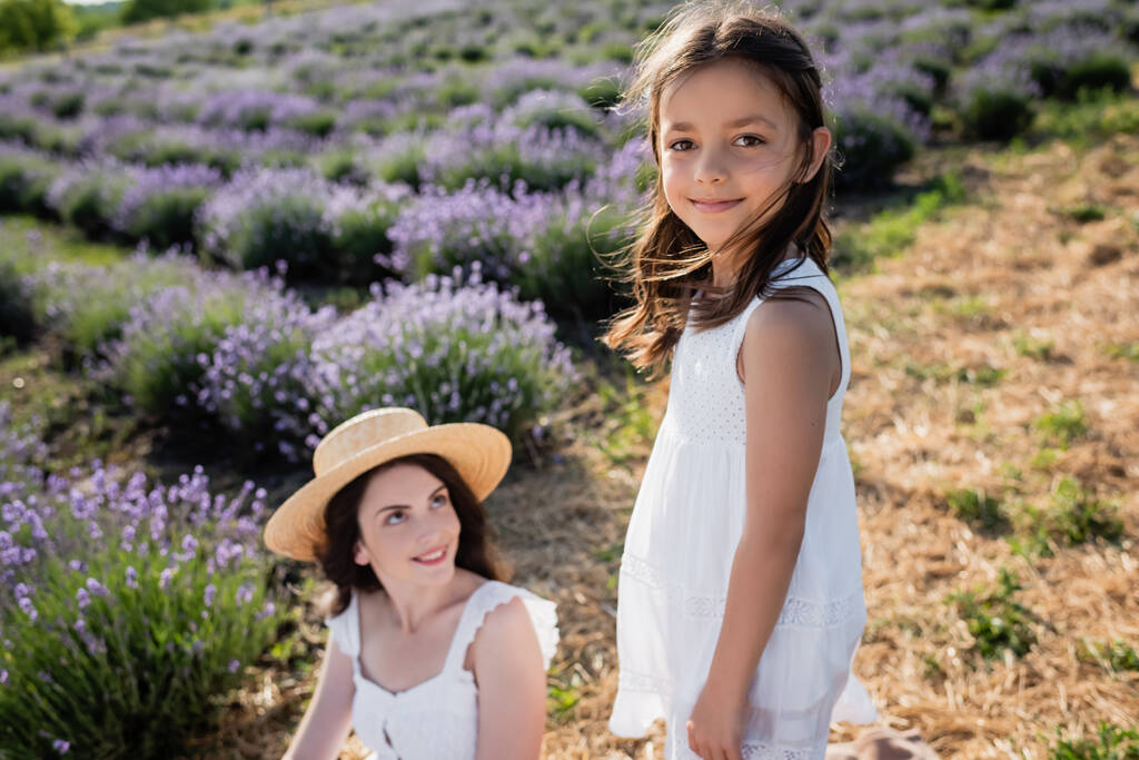 happy girl smiling at camera near blurred mom in lavender meadow - Foto, Imagem