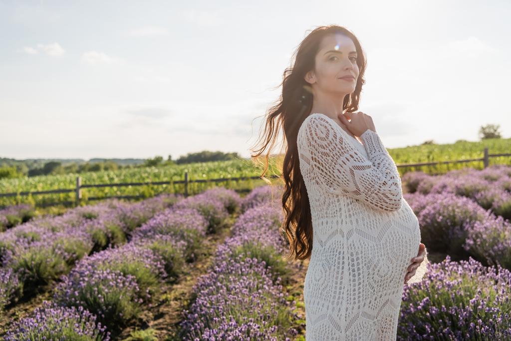 pregnant woman with long hair smiling at camera in lavender field - Photo, image