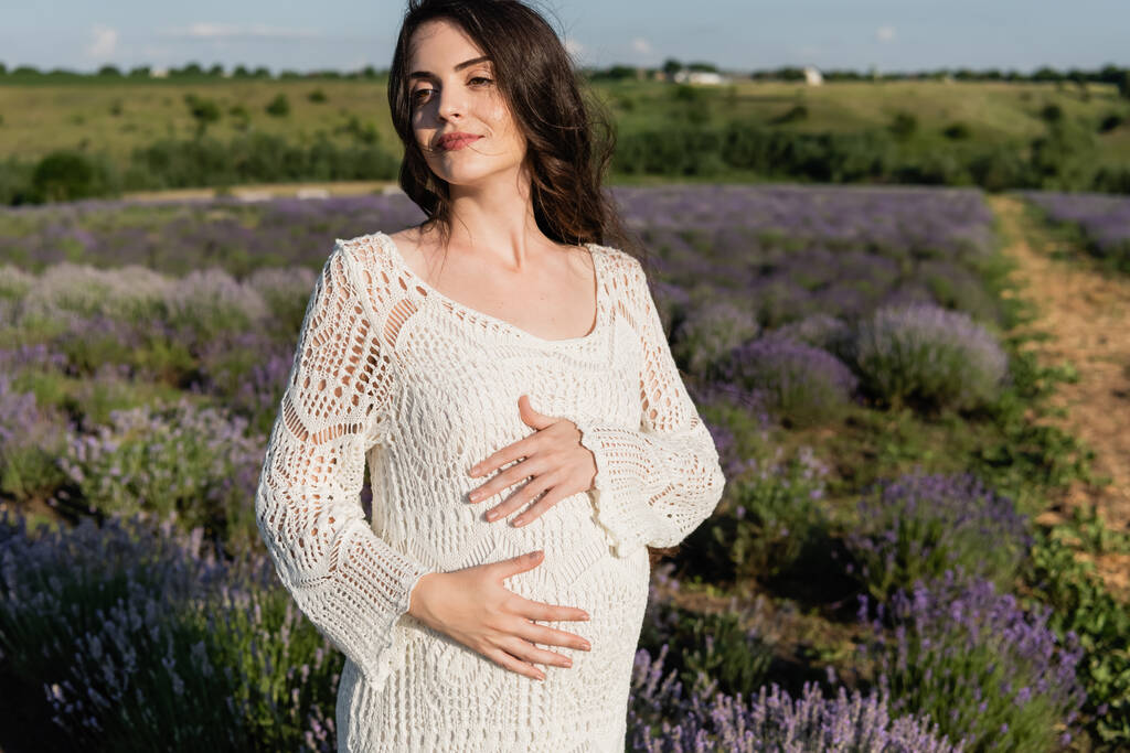 pregnant brunette woman in white dress in blurred field with blossoming lavender - Fotografie, Obrázek