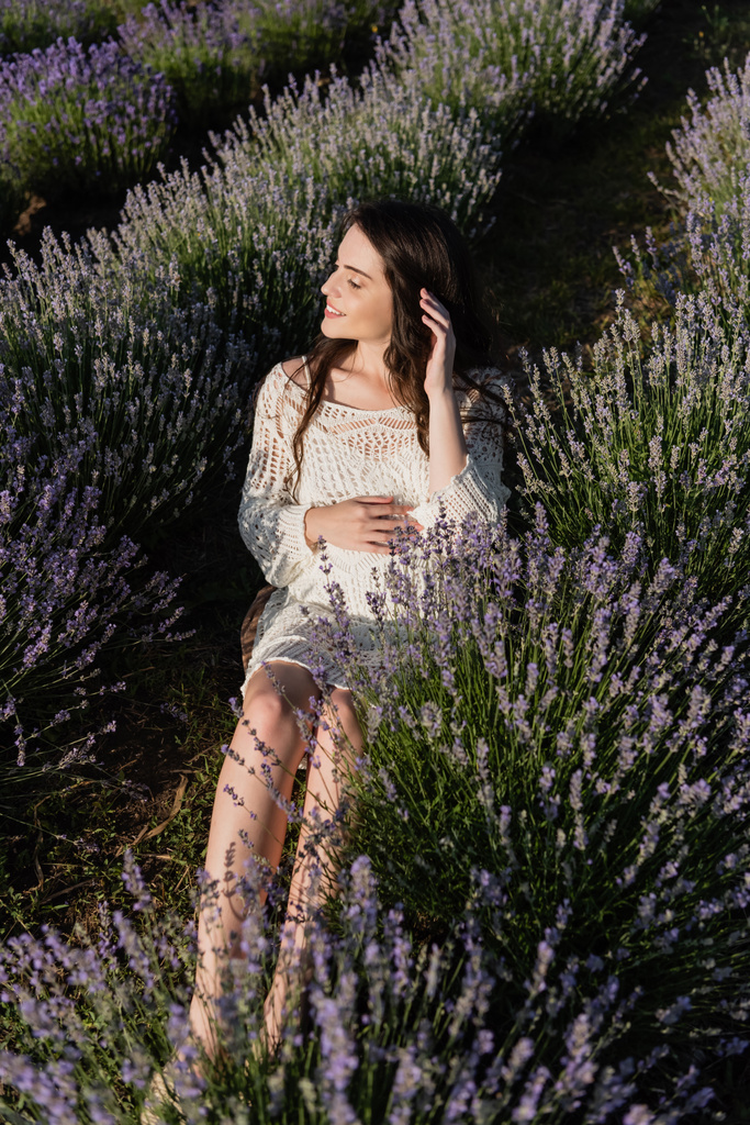 высокий угол обзора беременной женщины, сидящей рядом с цветущей лавандой в поле - Фото, изображение