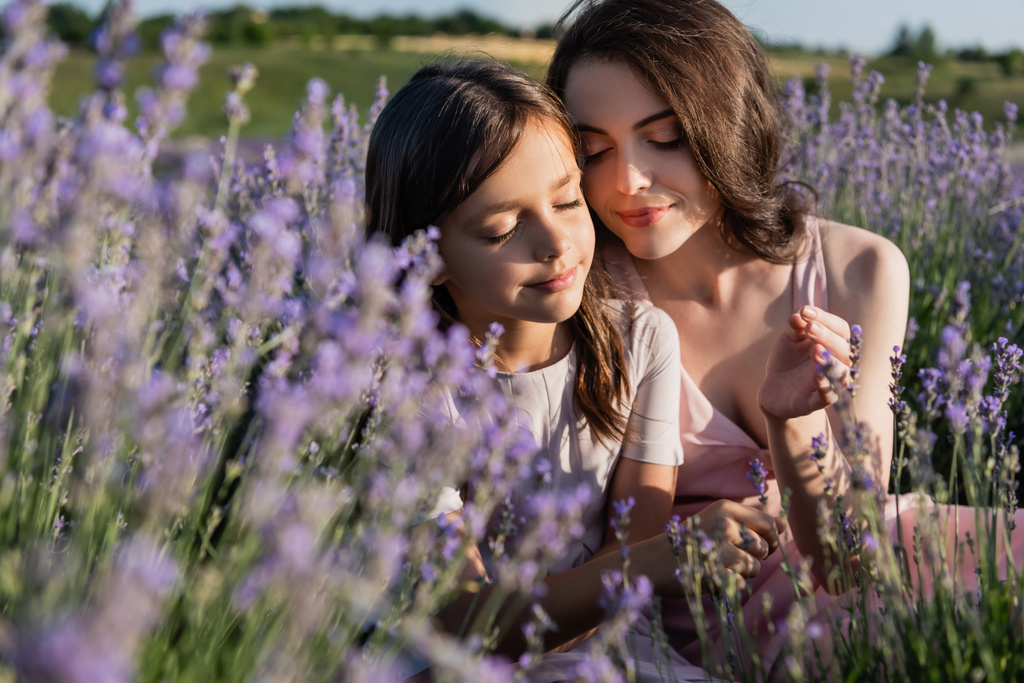 happy mom and daughter with long hair and closed eyes in blurred lavender field - Foto, afbeelding