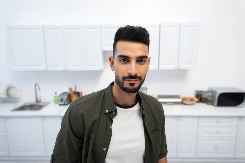 Young muslim man looking at camera in blurred kitchen  - Fotó, kép