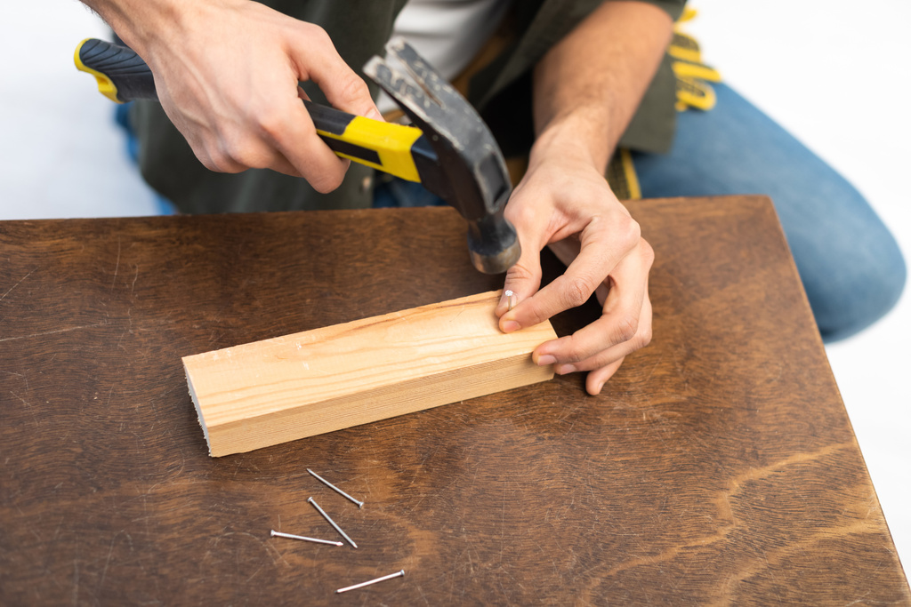 Cropped view of craftsman holding hammer and nail near wooden board on table  - Photo, Image