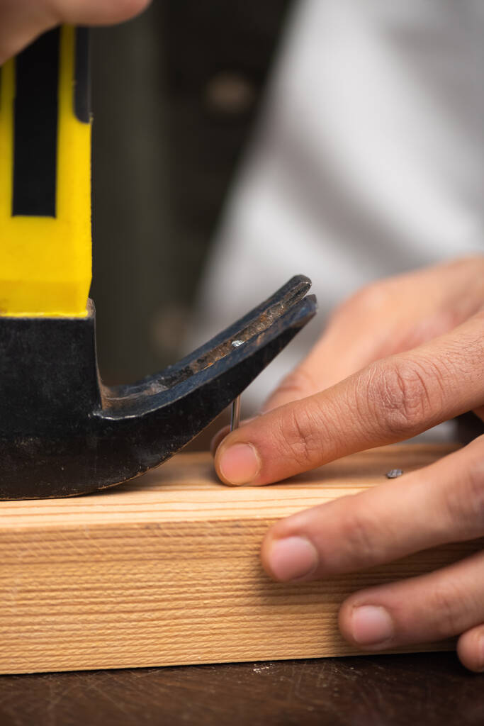 Cropped view of man picking up nail with manner near wooden board  - Foto, imagen