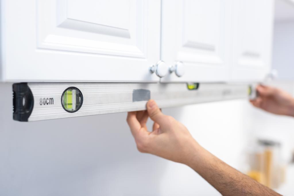 Cropped view of man holding spirit level near kitchen cabinet  - Photo, image