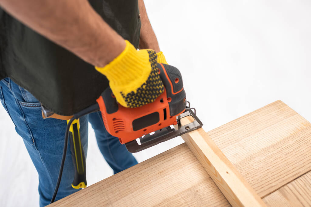 High angle view of man holding electric jigsaw machine near wooden plank at home  - Valokuva, kuva