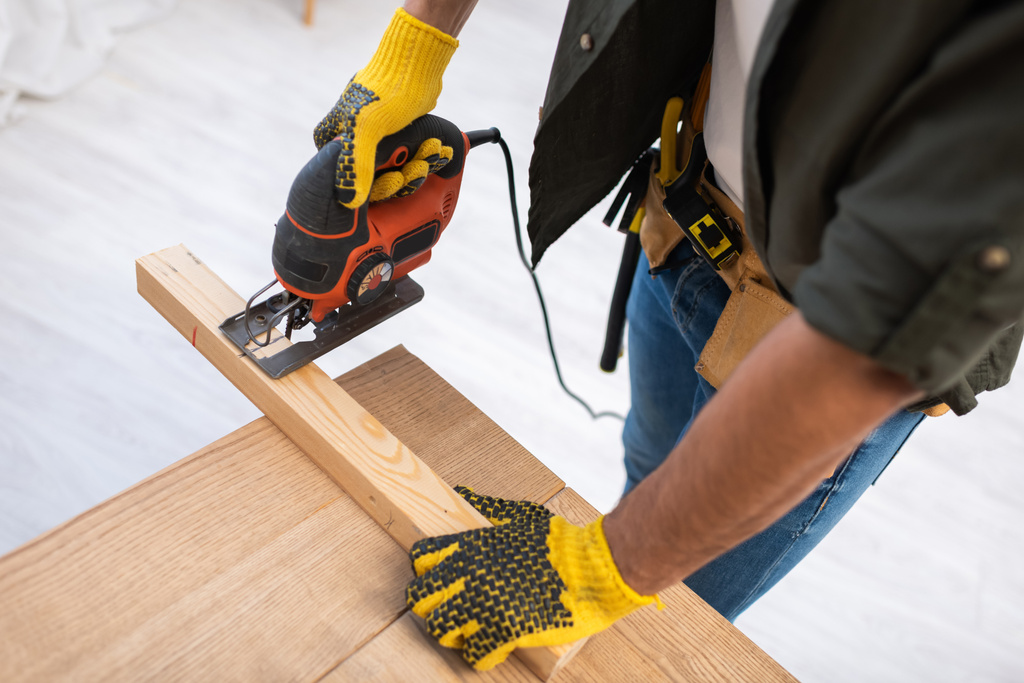 High angle view of carpenter in gloves sawing wooden board on table at home  - Valokuva, kuva