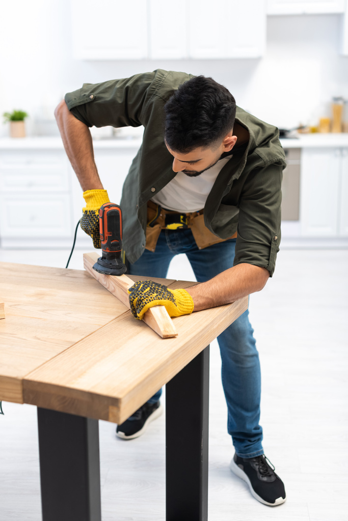 Arabian man in gloves sanding wooden board at home  - Photo, Image
