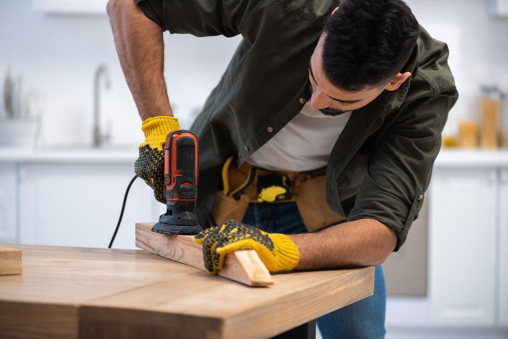 Muslim man with tool belt sanding wooden board at home  - Photo, image