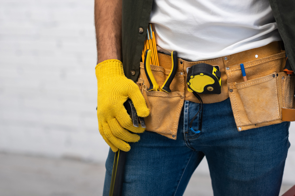 Cropped view of man in glove and tool belt holding hammer at home  - Valokuva, kuva