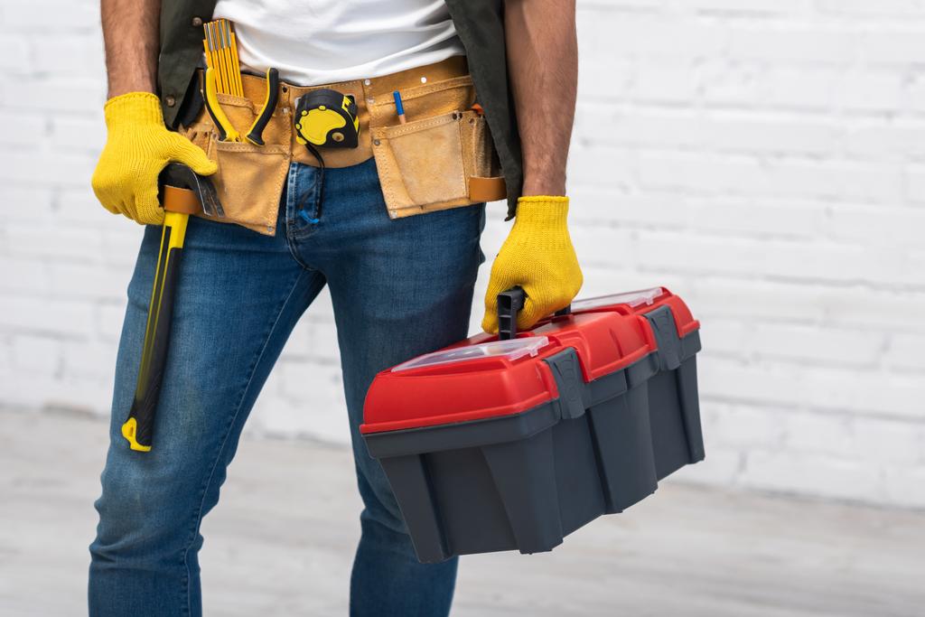 Cropped view of repairman in gloves and tool belt holding box at home  - Photo, image
