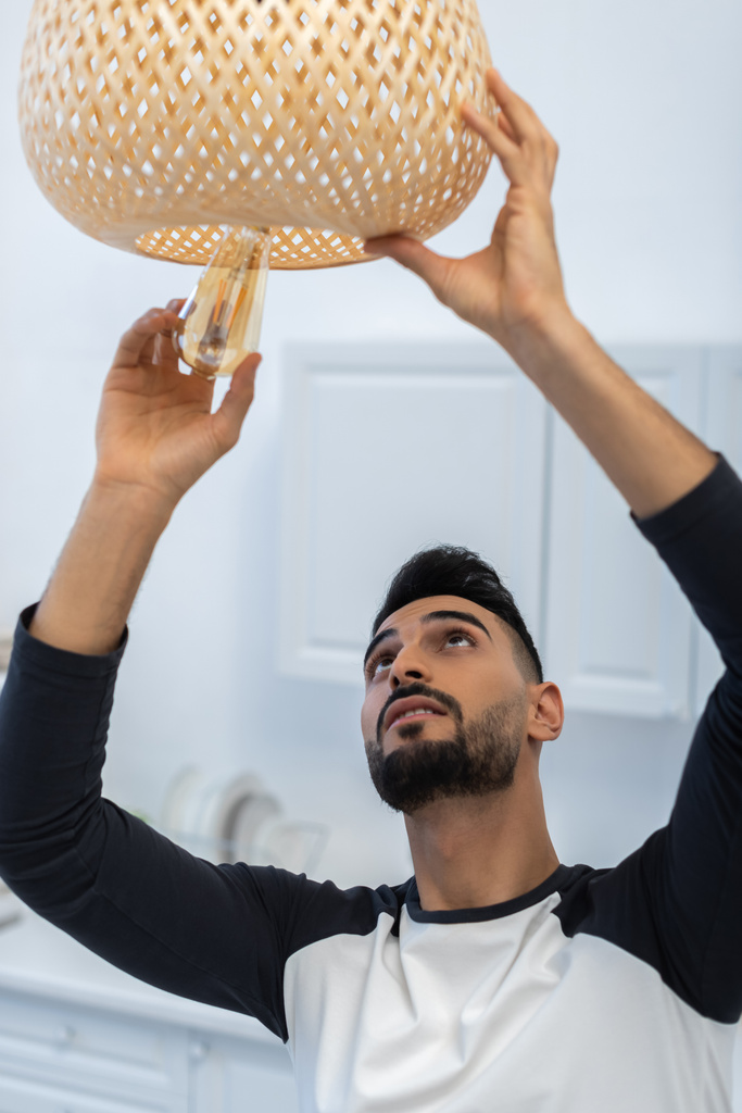 Muslim man holding lightbulb near chandelier in kitchen  - Foto, imagen