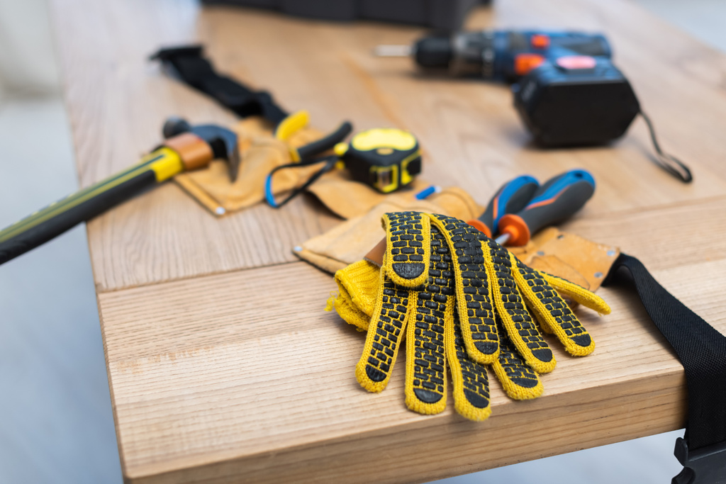 Gloves near blurred belt with tools on table at home  - Photo, Image