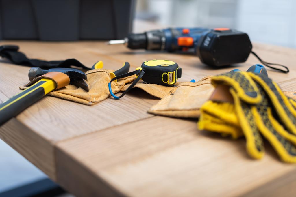 Hammer and tape measure on belt near blurred gloves on table  - Foto, immagini