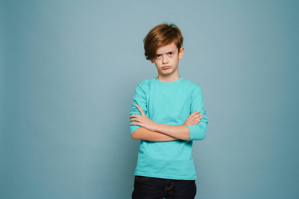 Ginger white boy frowning while posing with arms crossed isolated over blue wall - Valokuva, kuva
