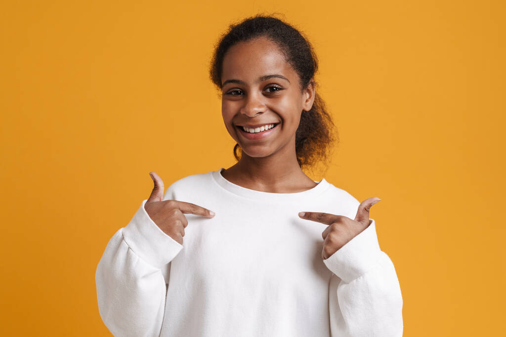 Brunette black girl smiling while pointing fingers at herself isolated over yellow background - Foto, Imagem