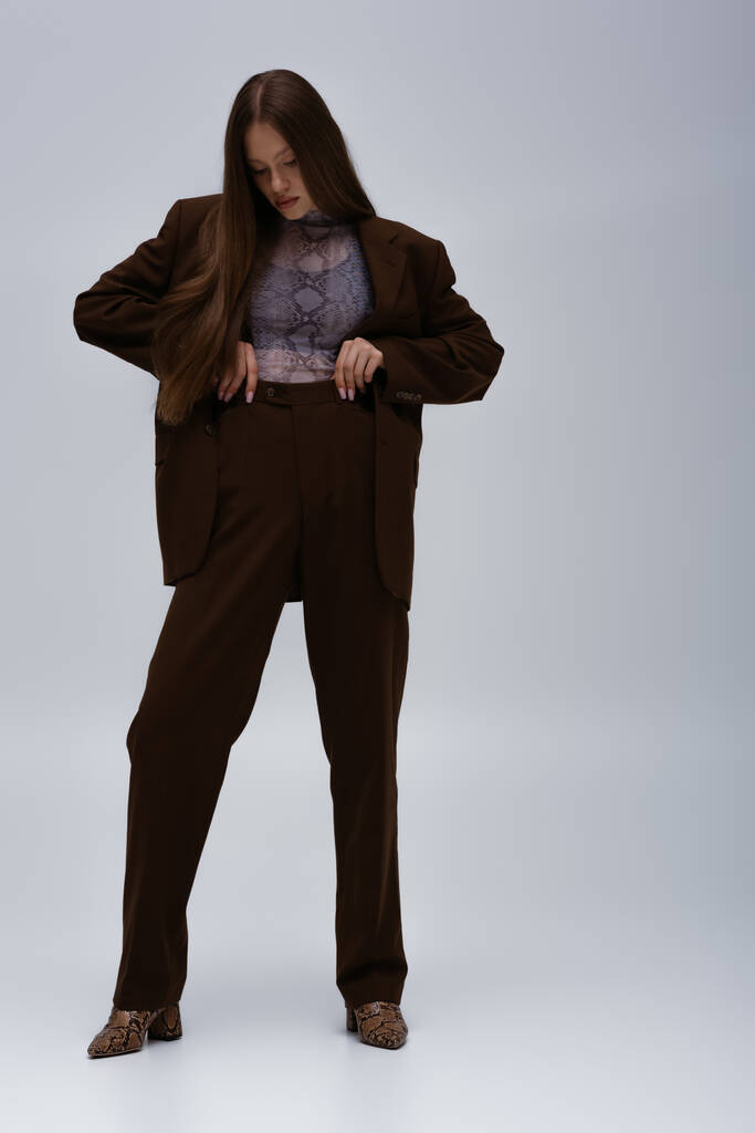 full length of teenage model in stylish high-quality suit adjusting trousers on grey - Valokuva, kuva