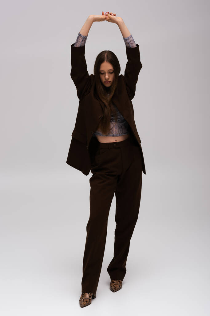 full length of teenage model in stylish high-quality suit posing with raised hands on grey - 写真・画像