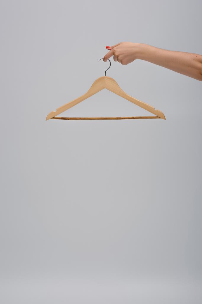partial view of woman holding wooden hanger isolated on gray - Fotografie, Obrázek