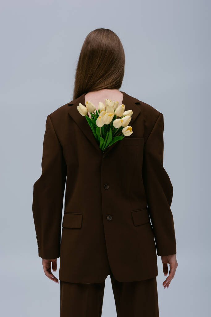 back view of teenage model in brown blazer with tulips isolated on grey - Foto, imagen