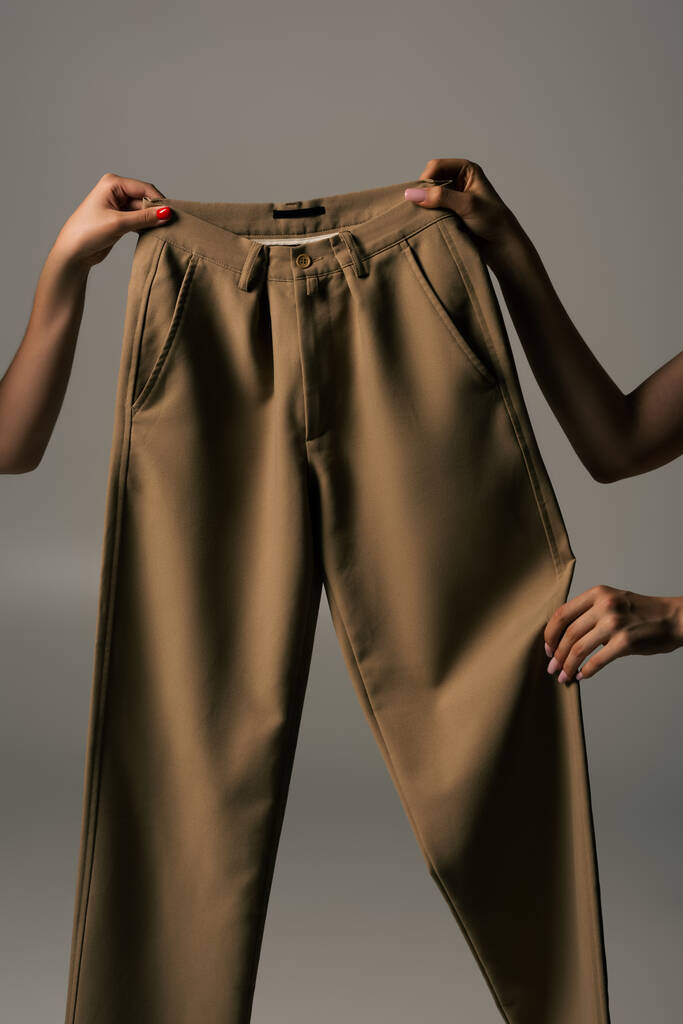 καλλιεργούμενη άποψη των γυναικών που κατέχουν ανακυκλώσιμα μπεζ παντελόνι απομονώνονται σε γκρι - Φωτογραφία, εικόνα