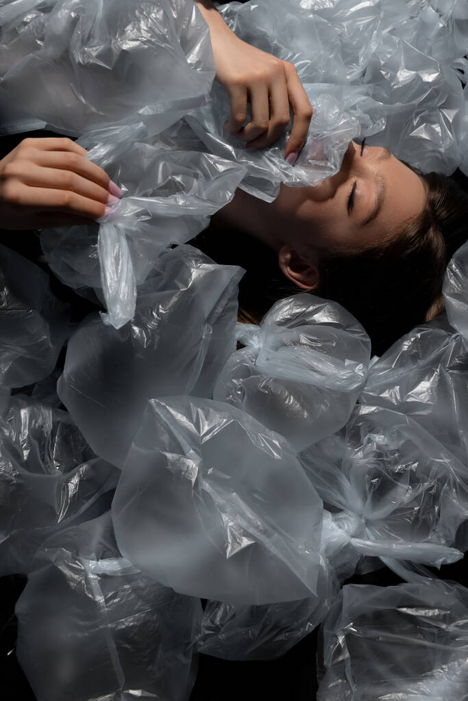 top view of model with closed eyes lying around plastic bags, recycle fashion concept - Foto, afbeelding