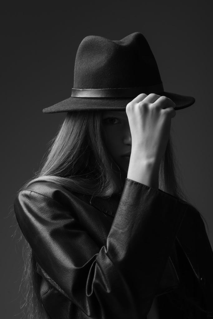 monochrome photo of model adjusting fedora hat in studio  - Zdjęcie, obraz