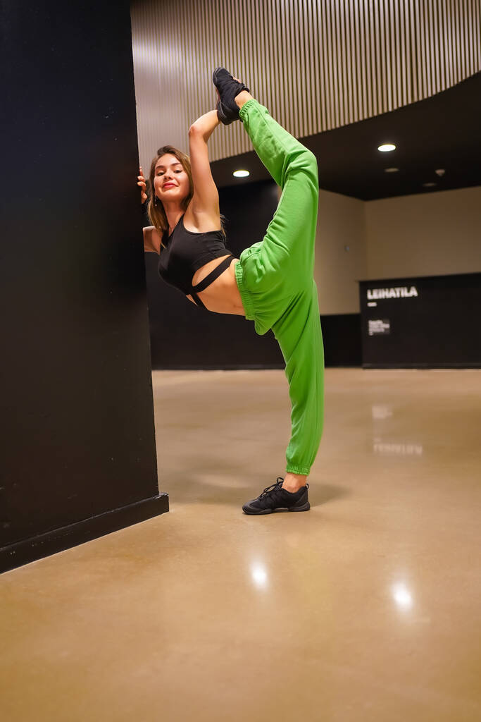 An urban and classical dancer woman inside a building, raising her leg on a wall and looking - Foto, Imagen