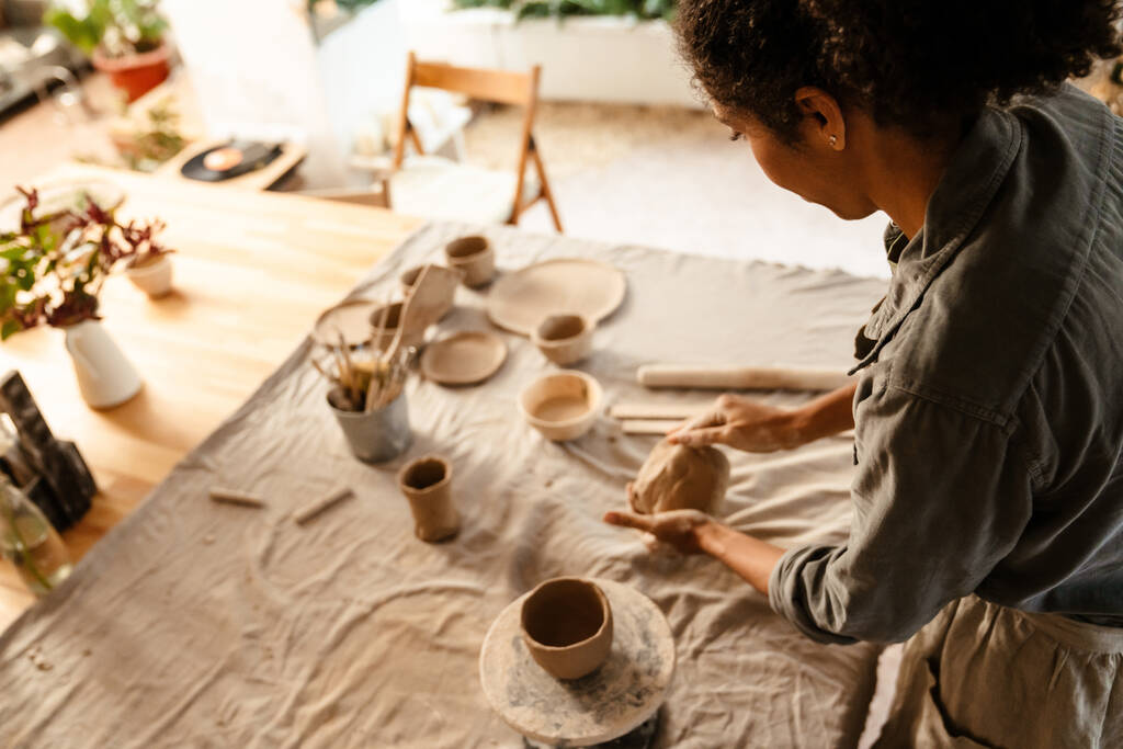 Young black ceramist woman wearing apron sculpting in clay at her workshop - Photo, image