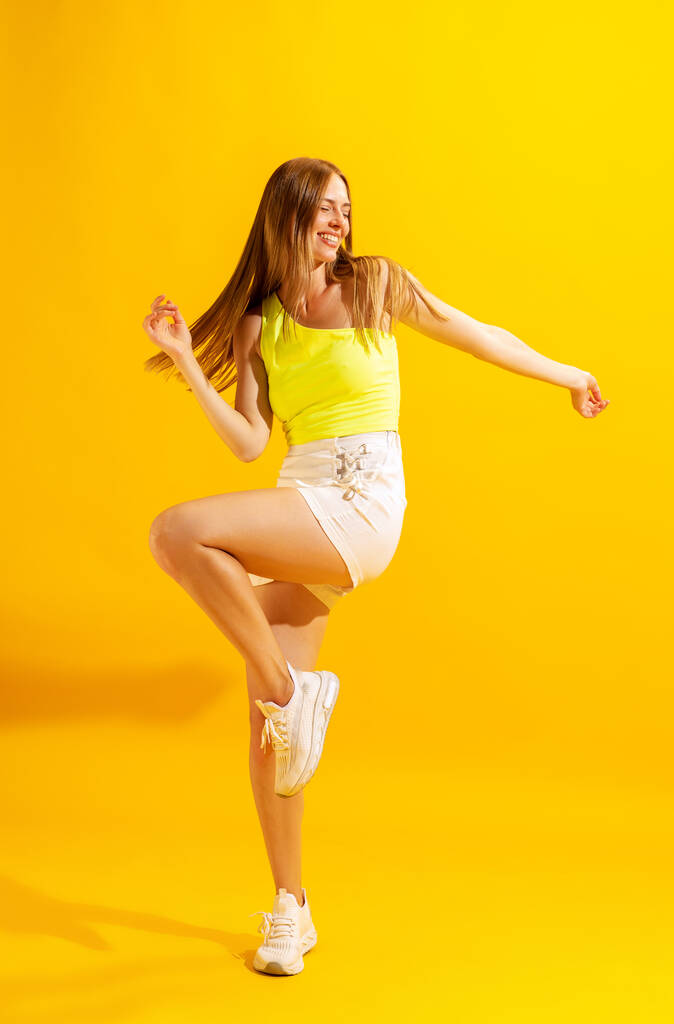 Enjoying freedom. Astonished young girl, student dancing isolated on bright yellow background. Concept of beauty, art, summer fashion, human emotions and facial expressions. Copy space for ad - Foto, immagini