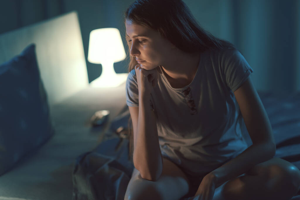 Tired young woman sitting on the bed late at night, sleep disorder concept - Photo, image