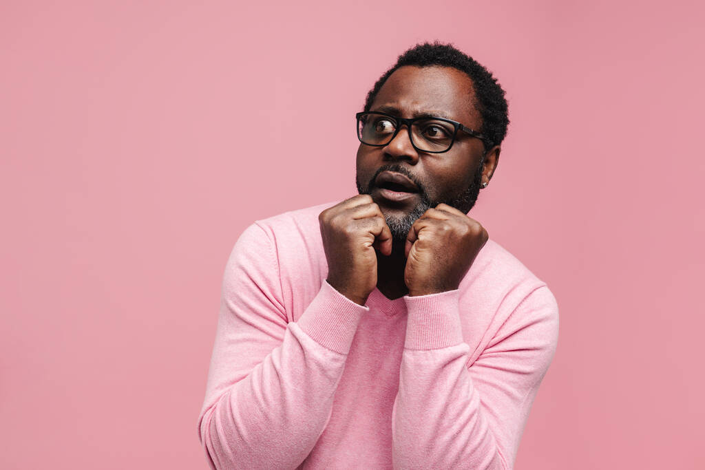 Black bearded man in eyeglasses expressing surprise at camera isolated over pink background - Foto, imagen