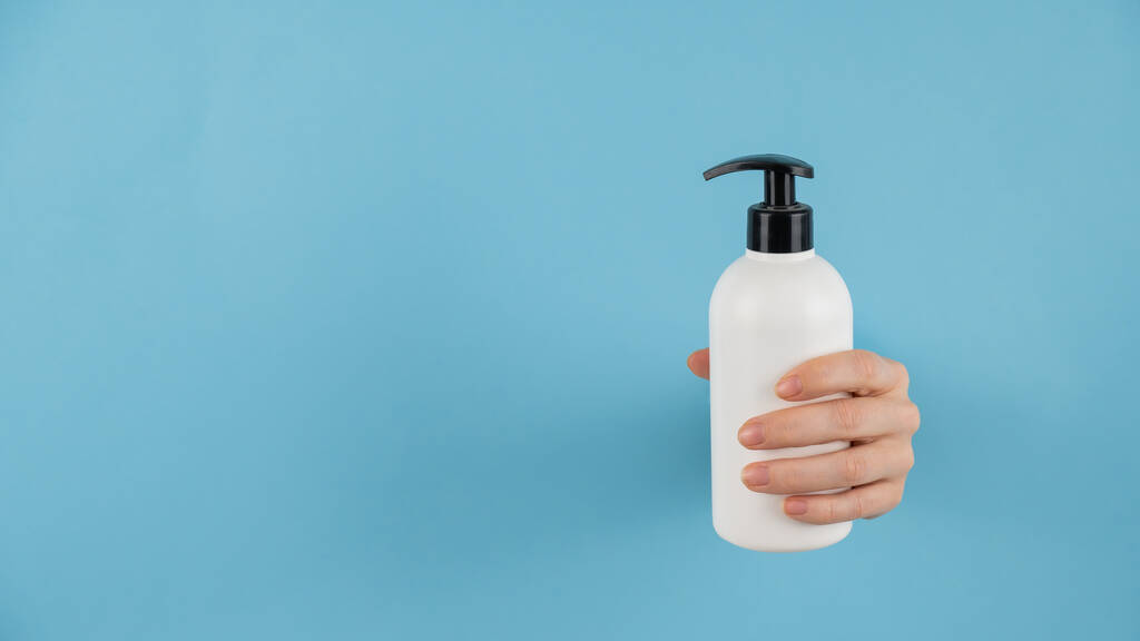 A womans hand sticks out of a hole in a blue paper background and holds a skin lotion pump - Photo, Image