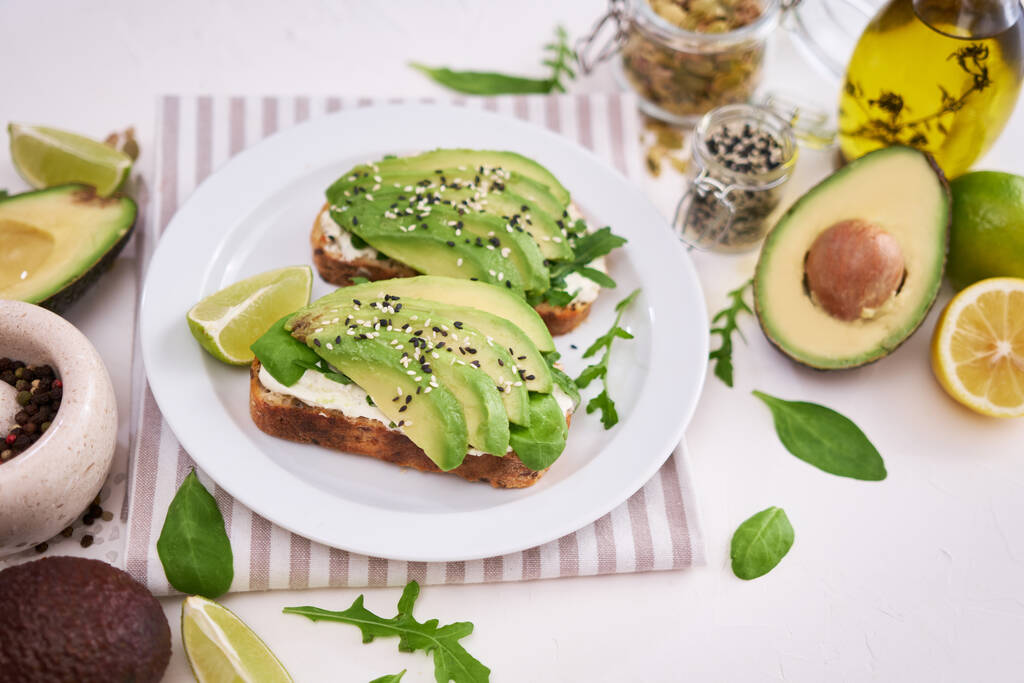 Freshly made Avocado and cream cheese toasts on a white ceramic plate and ingredients. - Foto, Imagen