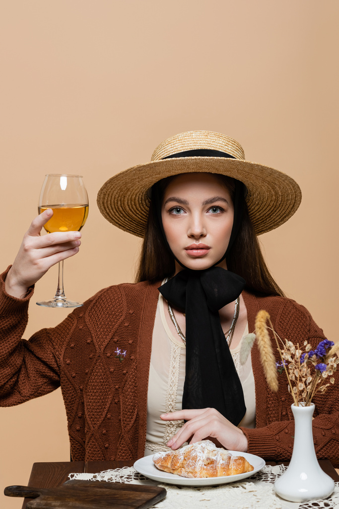 Young woman in sun hat holding glass of wine near food and plants isolated on beige  - Photo, Image