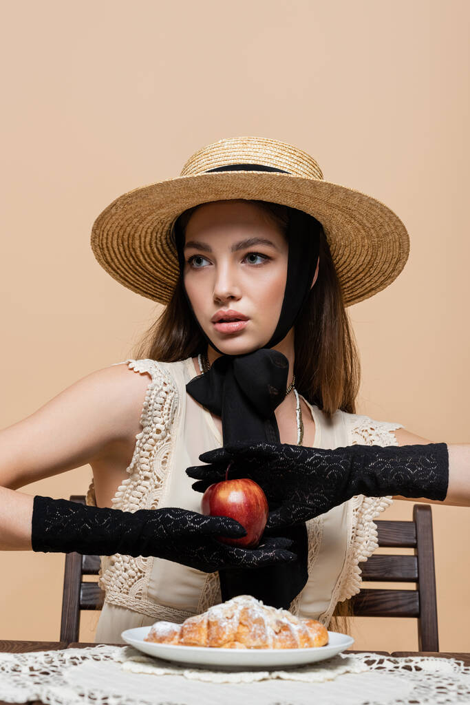 Fashionable woman in gloves holding apple near croissant isolated on beige  - Foto, Imagem