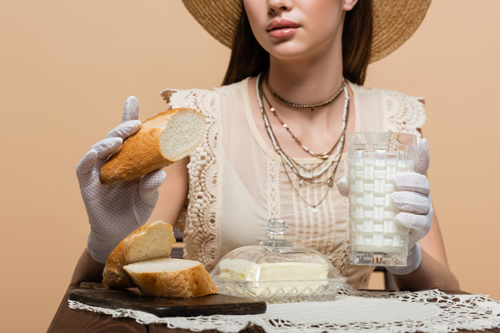 Cropped view of young woman in gloves holding bread and milk near butter isolated on beige  - Foto, Imagem