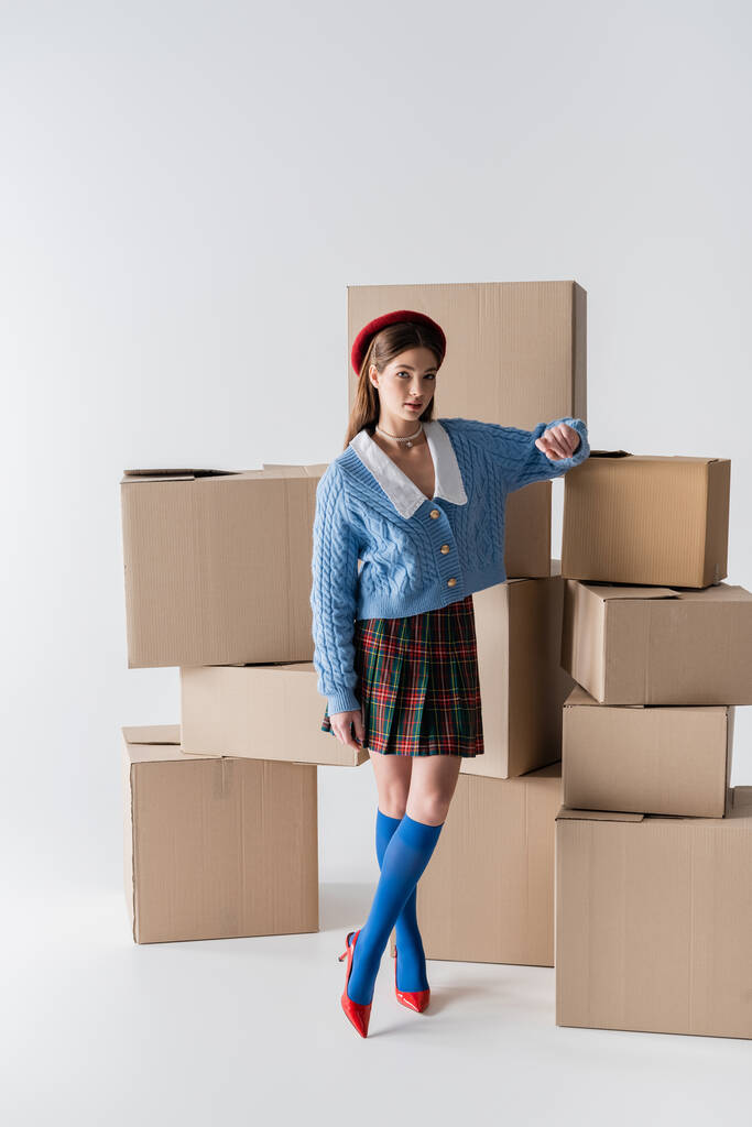 Full length of trendy model standing near carton boxes on white background  - Foto, immagini