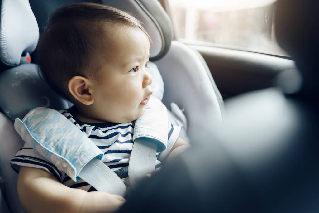 szczęśliwy Azji chłopiec w foteliku samochodowym, mały maluch podróży samochodem z rodziną. - Zdjęcie, obraz