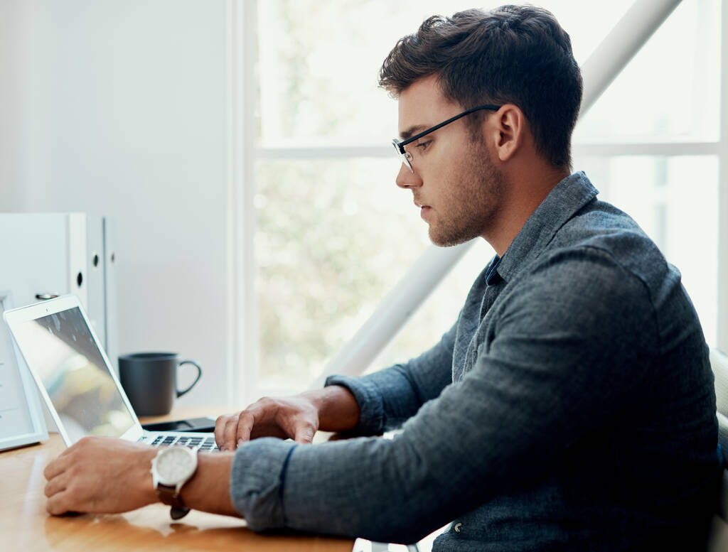 Помогаю клиентам в сети. красивый молодой бизнесмен, сидящий один и пользующийся своим ноутбуком в офисе - Фото, изображение
