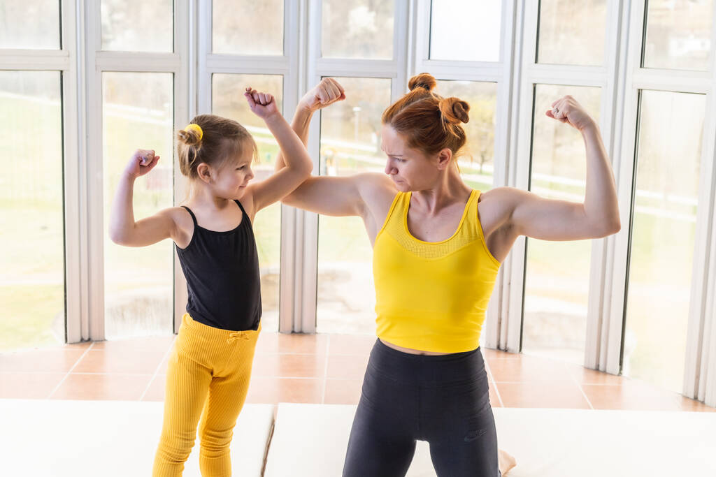 Young fit mom and her daughter in matching clothes, showing muscles. Fitness motivation - Photo, Image